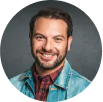Hair Transplant - a bearded man with a nice head of hair is wearing a plaid button-up shirt and a jean jacket - he is smiling directly at the camera.