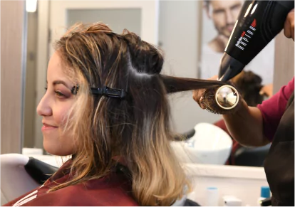 HairClub - EXT Scalp Treatments - a woman sitting in a HairClub salon getting her hair blown dry and styled by a professional HairClub stylist.
